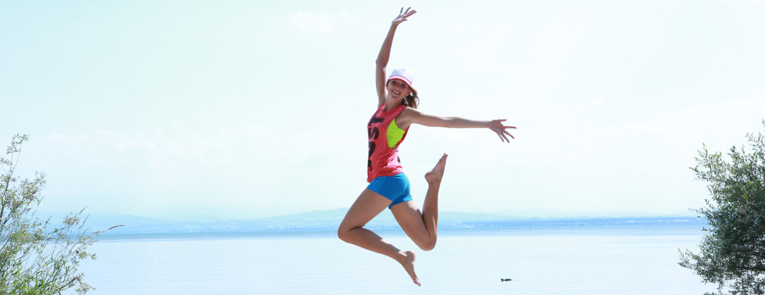 Junge Frau springt am See in die Luft